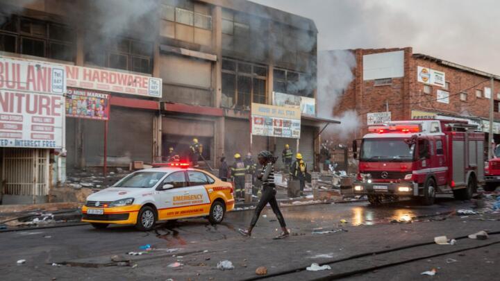 A woman walks past a fire truck as it extinguishes flames in a looted store in Alexandra township, Johannesburg, South Africa, on July 12, 2021.